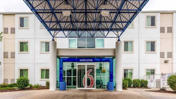Een modern gebouw met een blauw entreekap en een bord met de tekst 'welcome', plus een groot nummer '6'.
