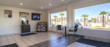 A hotel lobby with a reception desk, a digital screen, a magazine rack, and a view of the parking area.
