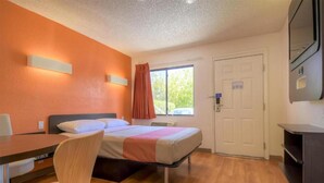 Habitación de hotel con cama, escritorio, silla, televisión y ventana con cortinas.