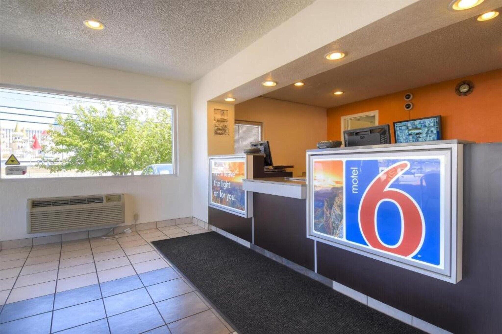 A motel reception desk with a large sign indicating room number 6, a window with blinds, and a tiled floor.