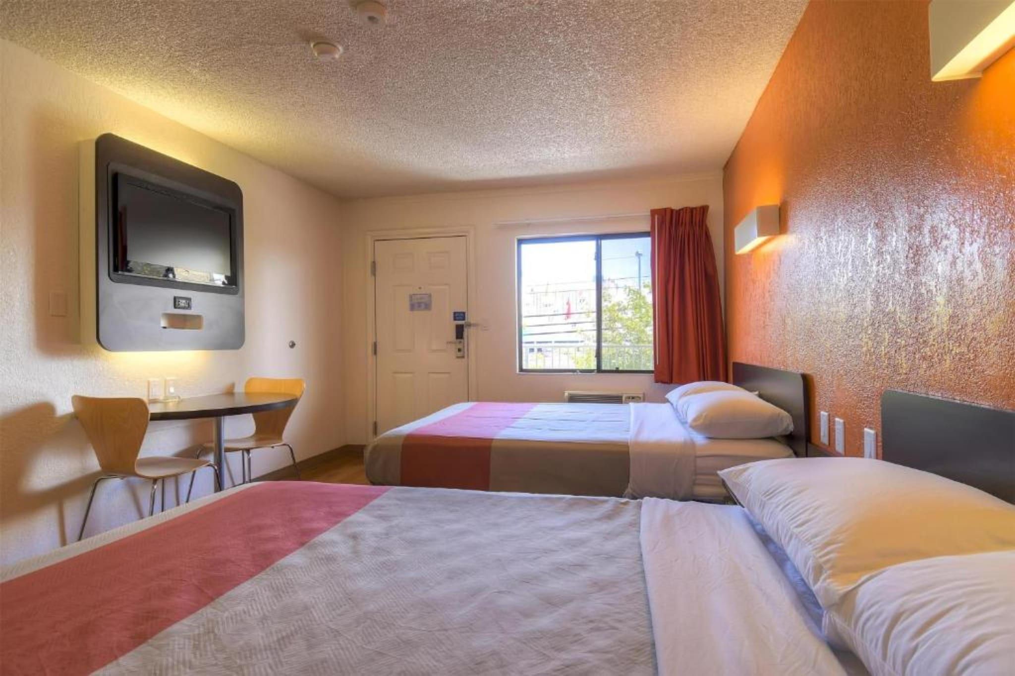 Habitación de hotel con dos camas, un escritorio, una silla, una ventana con cortinas y un televisor de pared.