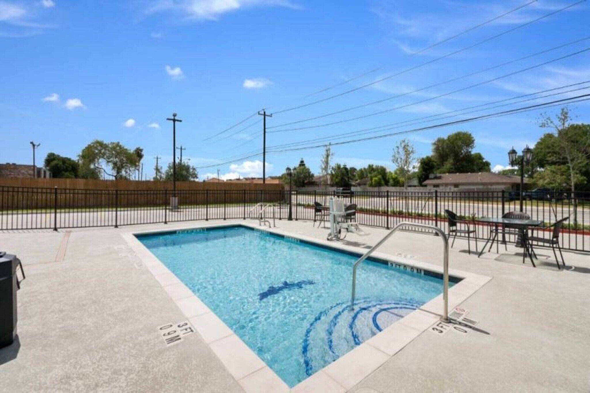 A rectangular swimming pool with a metal ladder, surrounded by a fence, and a trash bin nearby.