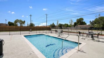 A rectangular swimming pool with a metal ladder, surrounded by a fence, and a trash bin nearby.