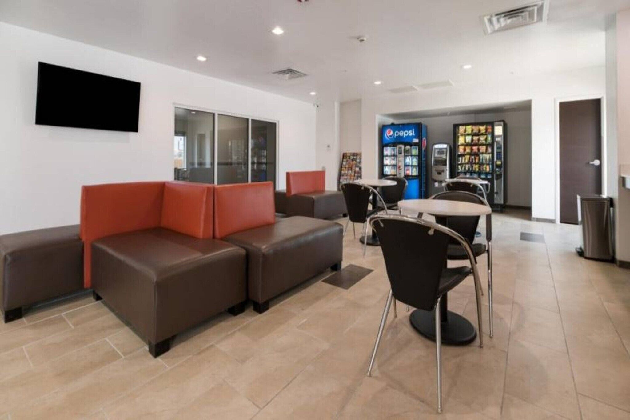 A modern waiting area with leather sofas, a flat-screen TV, and a Pepsi vending machine.