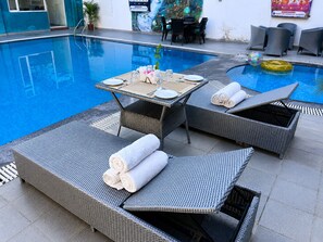 Zona junto a la piscina con sillones de mimbre, una mesa lista para comer y una piscina inflable pequeña.