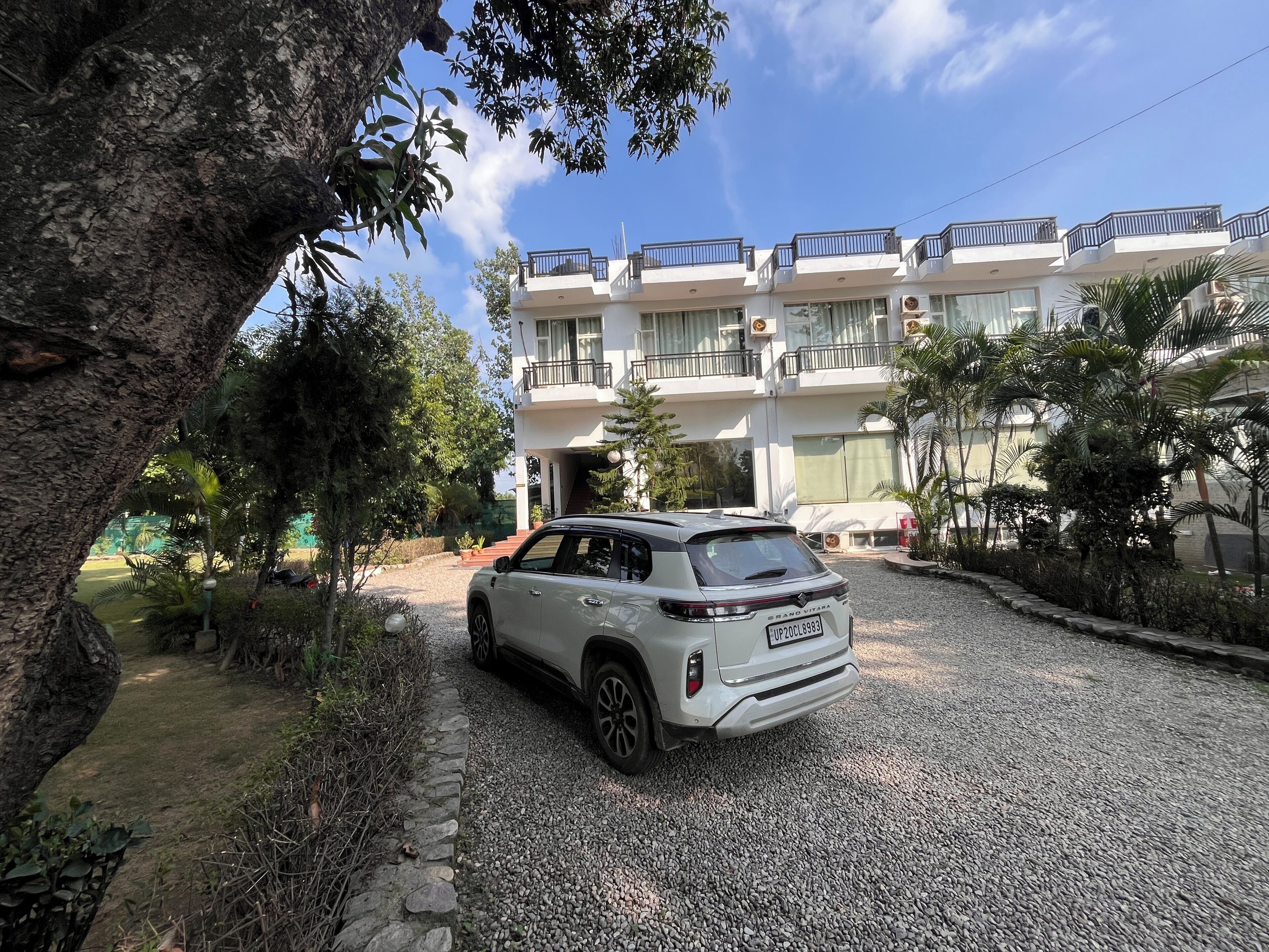 A white SUV parked in a gravel driveway with a multi-story building in the background.