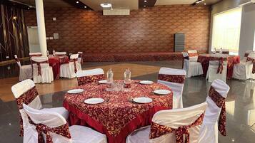 A banquet hall with round tables covered in red tablecloths, white chairs with red sashes, and a brick wall in the background.