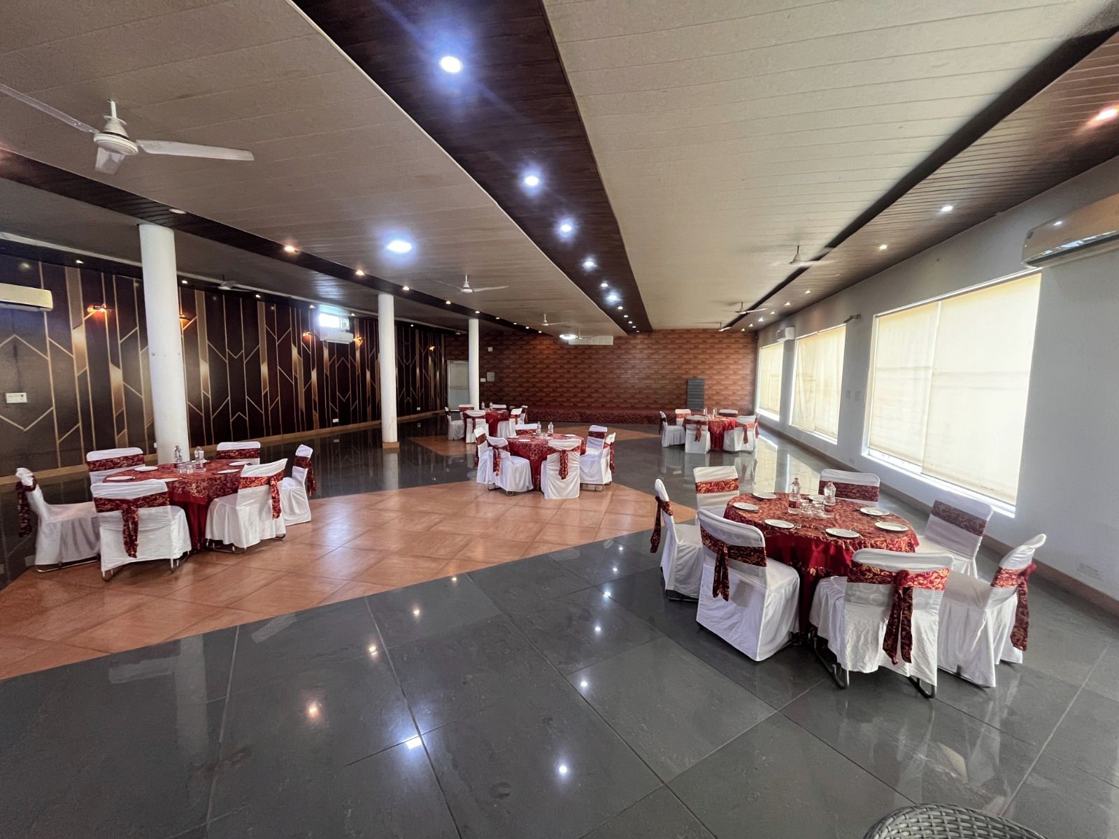 A spacious hall with multiple round tables, white chairs, and red tablecloths.