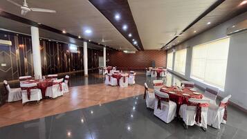 A spacious hall with multiple round tables, white chairs, and red tablecloths.