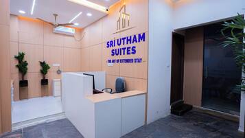 A reception desk with a sign for Sri Utham Suites. There is a ceiling fan, a plant, and a wall-mounted air conditioner.
