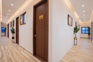 A hotel corridor with wooden doors, potted plants, and artwork on the walls. - Sri Utham Suites (Bengaluru)