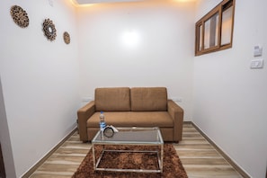 A living room with a brown sofa, a glass coffee table, and decorative wall art. - Sri Utham Suites (Bengaluru)