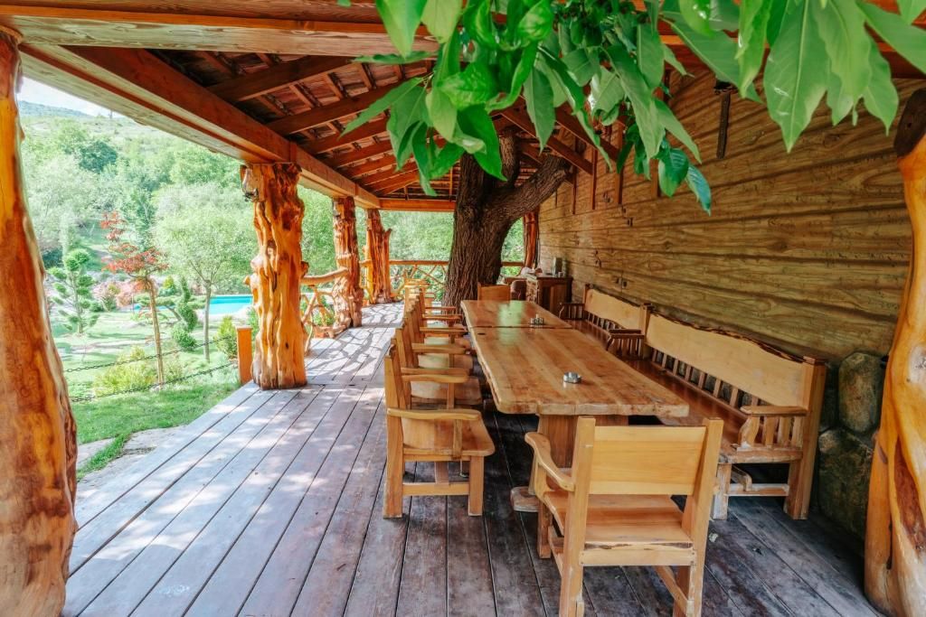 A wooden deck with a long table and benches, surrounded by a wooden wall and a large tree.