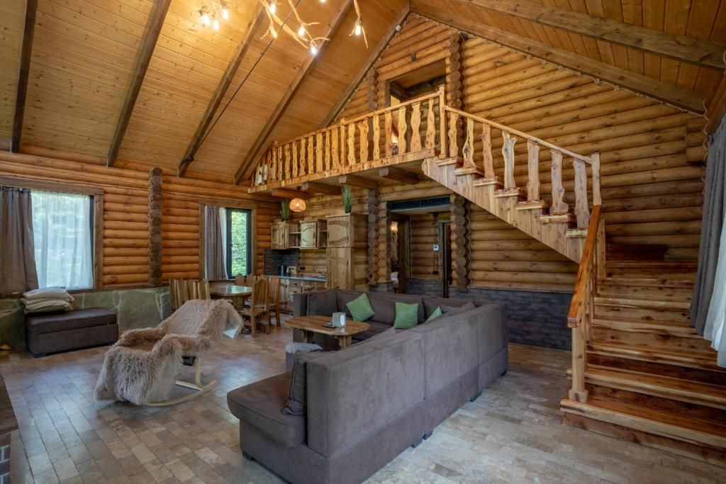 A log cabin interior with a wooden staircase, a sofa, and a rocking chair.