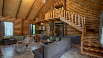 A log cabin interior with a wooden staircase, a sofa, and a rocking chair.