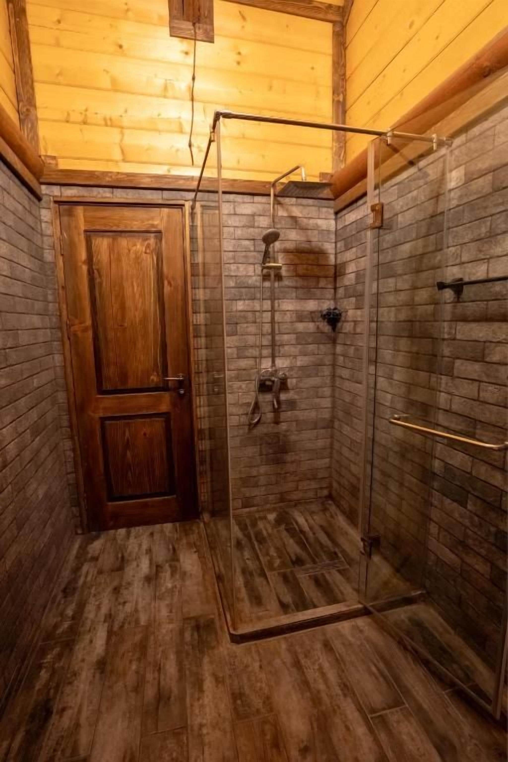 Ein Badezimmer mit Holzwänden, einer Glasdusche, einer Holztür und einem gefliesten Boden.