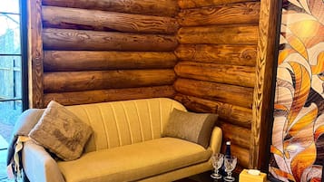 L'intérieur d'une cabane en rondins, avec un canapé, une table en verre sur laquelle se trouvent une bouteille et des verres, et un vitrail.