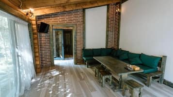 Ein Holzinnenraum mit einer Ziegelwand, einem grünen Sofa und einem Holztisch mit Bänken.