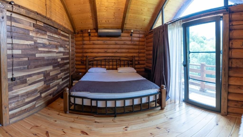 A log cabin bedroom with a bed, a window, and a view of the outdoors.