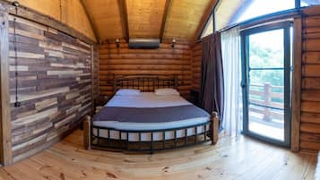A log cabin bedroom with a bed, a window, and a view of the outdoors.