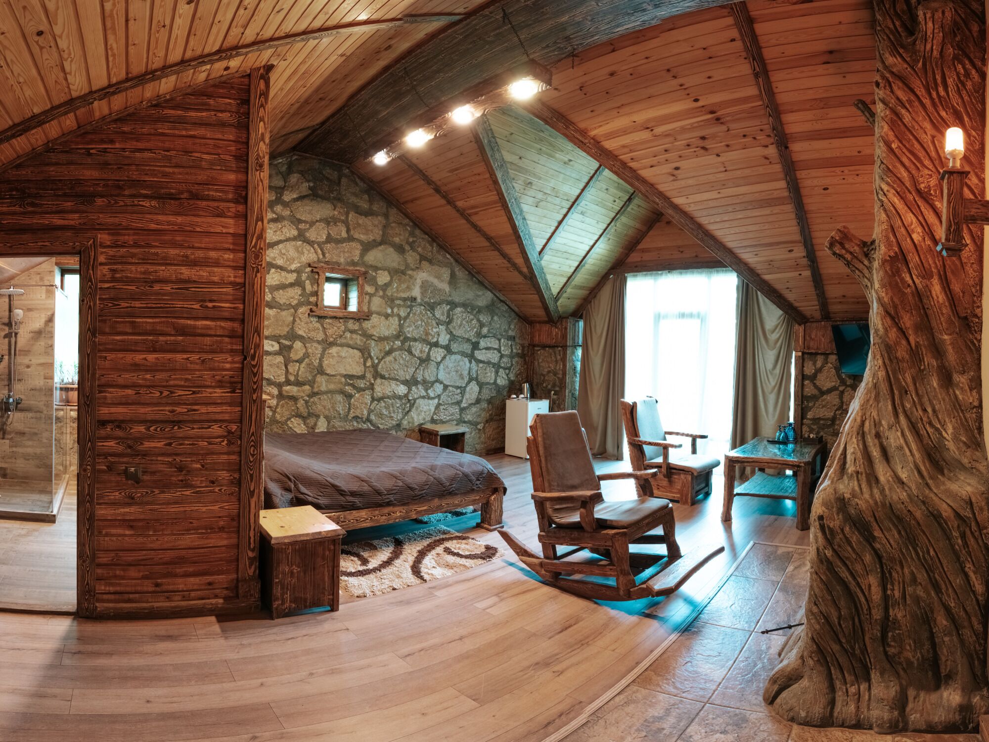 Un dormitorio rústico con pared de piedra, techo de madera y una cama grande.