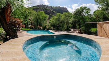 A swimming pool with a tiled edge, surrounded by greenery and a mountain in the background.