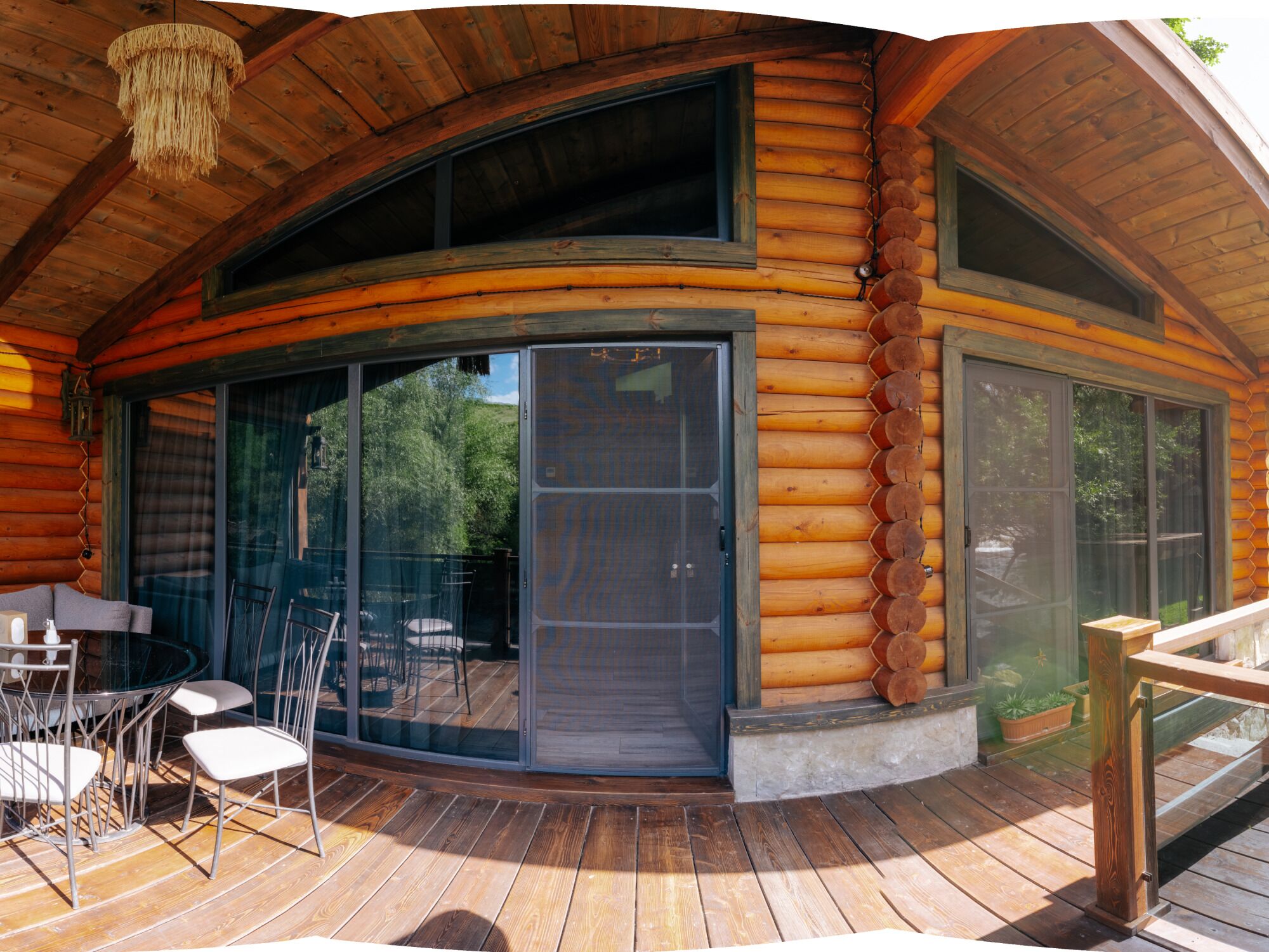 A log cabin with a glass door entrance, outdoor seating, and a wooden deck.