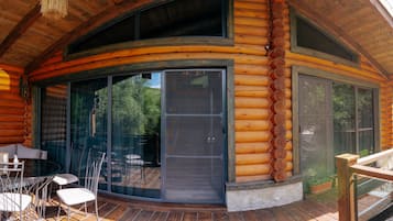 A log cabin with a glass door entrance, outdoor seating, and a wooden deck.