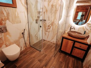 A bathroom with a glass-enclosed shower, a wooden vanity with a marble sink, and a toilet.