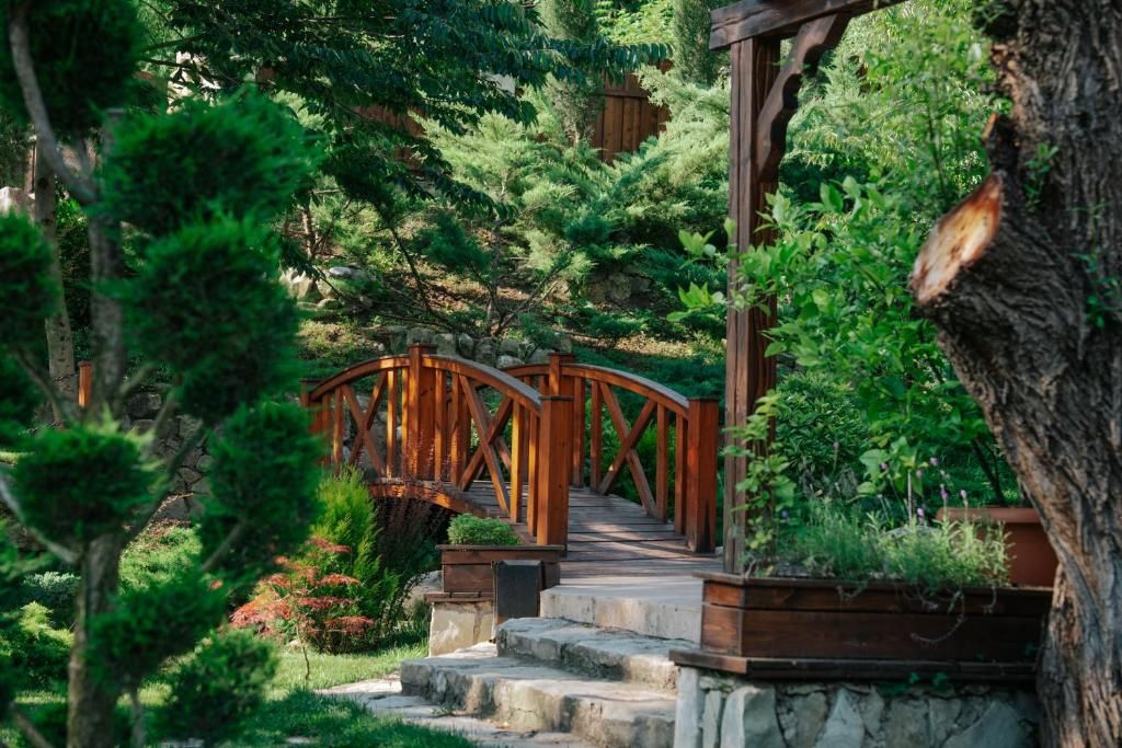 A wooden bridge leading to a stone staircase in a lush garden with dense foliage.
