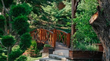 A wooden bridge leading to a stone staircase in a lush garden with dense foliage.