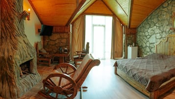 Une chambre à coucher rustique avec une cheminée en pierre, un fauteuil à bascule en bois et un lit recouvert d’une courtepointe.