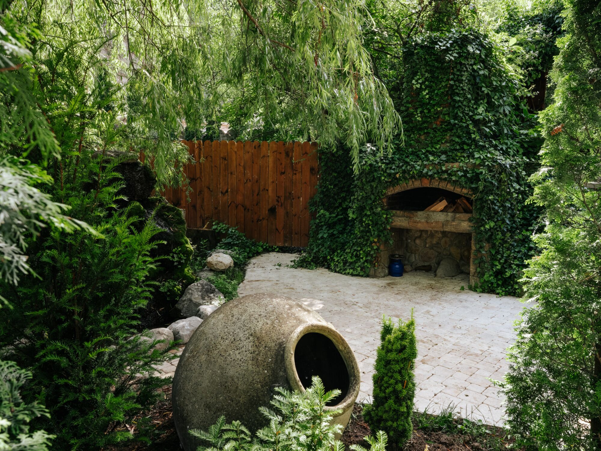 Um jardim com um canteiro de pedra, cerca de madeira e uma estrutura de pedra em arco.