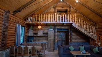A log cabin interior with a dining area, a sofa, and a staircase.