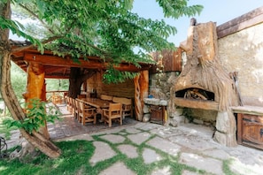 Un patio exterior con una pérgola de madera, piso de piedra y una rústica chimenea de piedra.