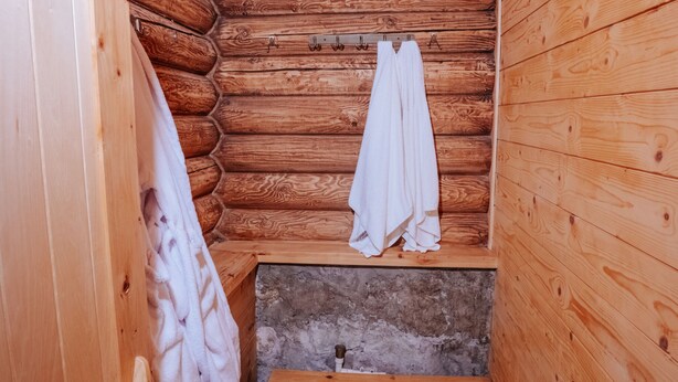 Interior de una cabaña de madera con un banco, perchero y pared de piedra.