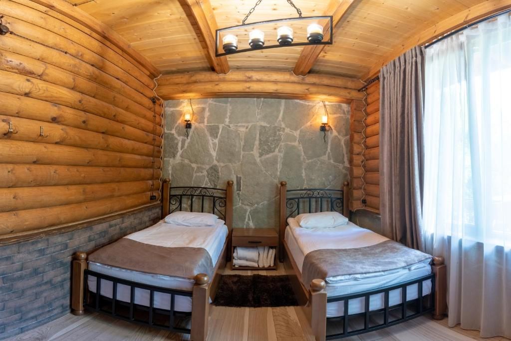 A log cabin room with two beds, stone walls, and a wooden ceiling.