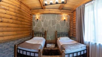 A log cabin room with two beds, stone walls, and a wooden ceiling.