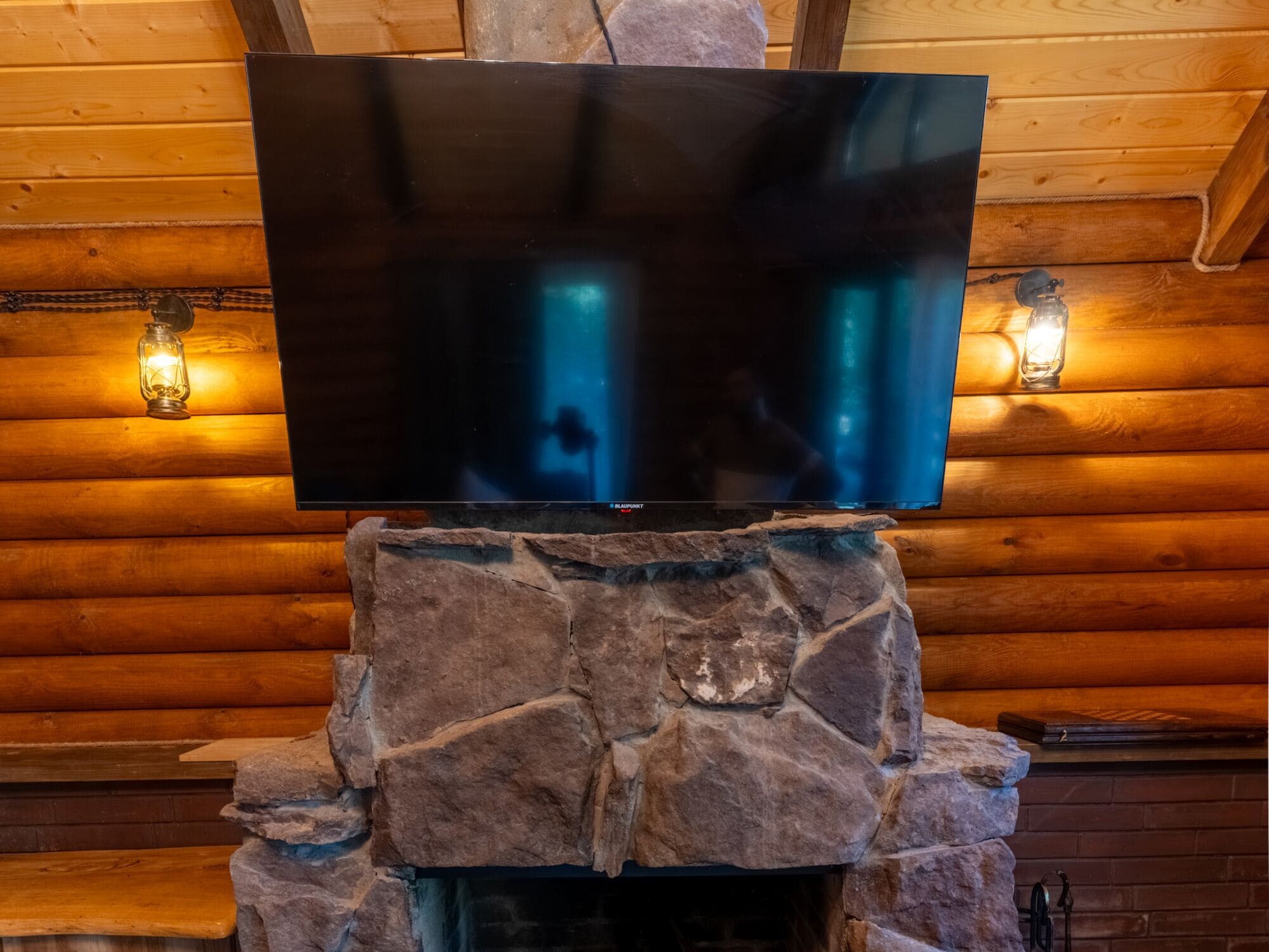 Un televisor de pantalla plana montado en una chimenea de piedra en una cabaña de troncos.