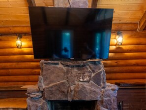 Un televisor de pantalla plana montado en una chimenea de piedra en una cabaña de troncos.