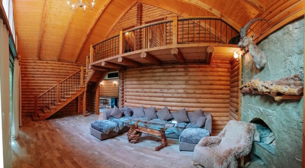 A log cabin interior with a staircase, a sofa set, and a stone fireplace.