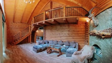A log cabin interior with a staircase, a sofa set, and a stone fireplace.