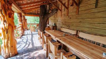 A wooden cabin with a long dining table and benches, surrounded by large trees.