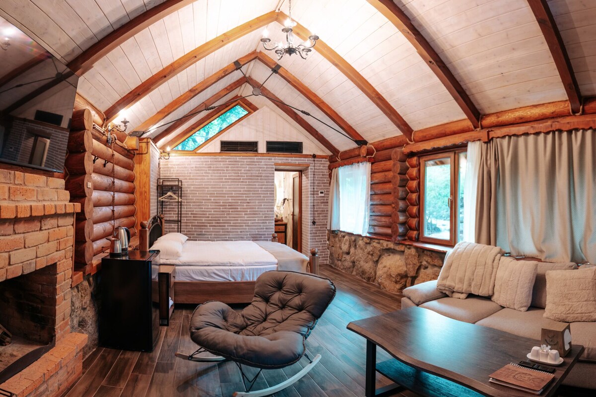 A log cabin interior with a loft bedroom, a fireplace, a sofa, and a dining table.