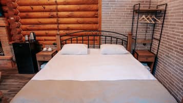 Una cama doble con cabecera de madera, una mesita de noche con tetera y un perchero.
