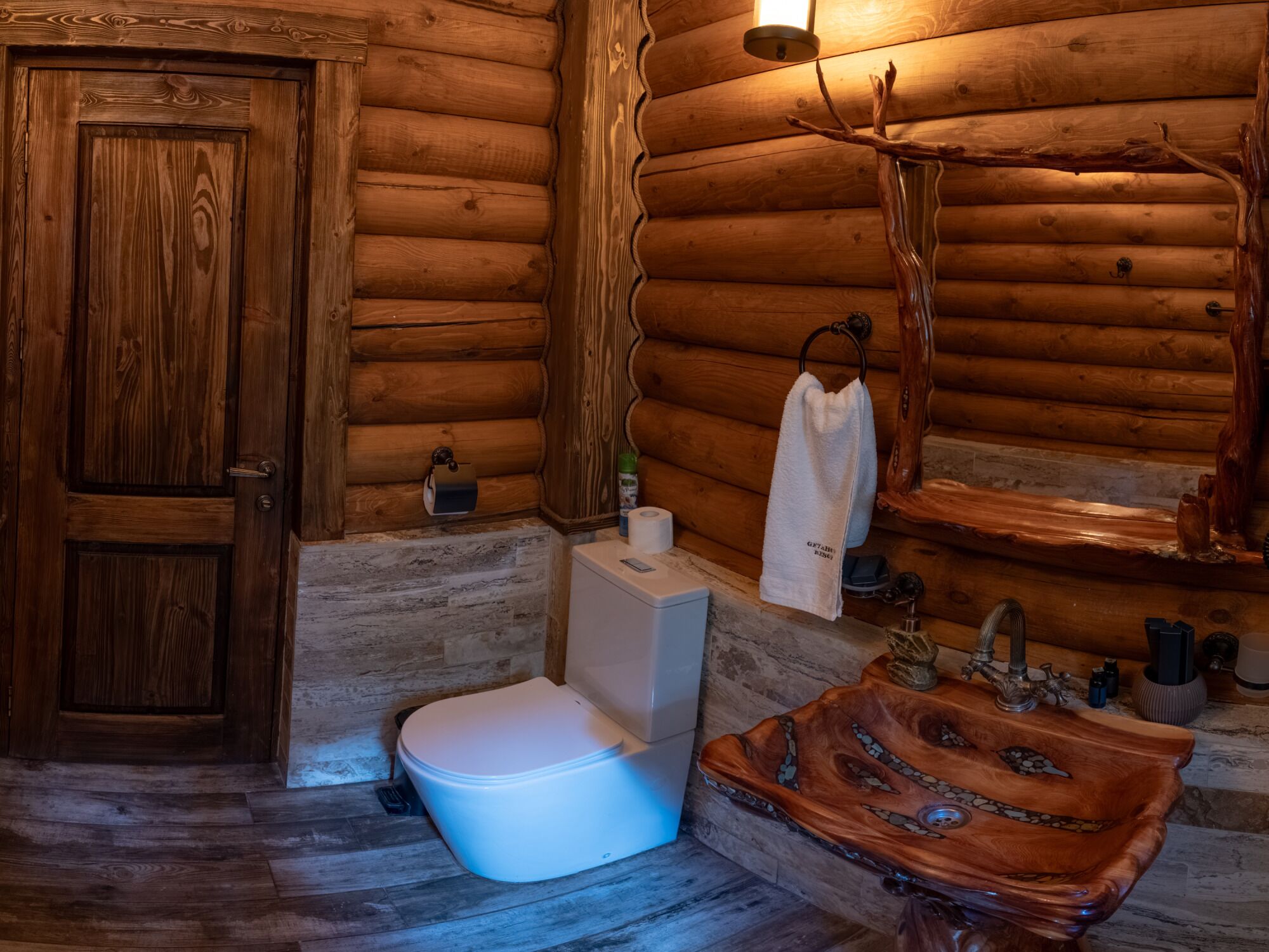 A wooden cabin bathroom with a toilet, sink, and a wooden shelf with toiletries.