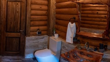 A wooden cabin bathroom with a toilet, sink, and a wooden shelf with toiletries.