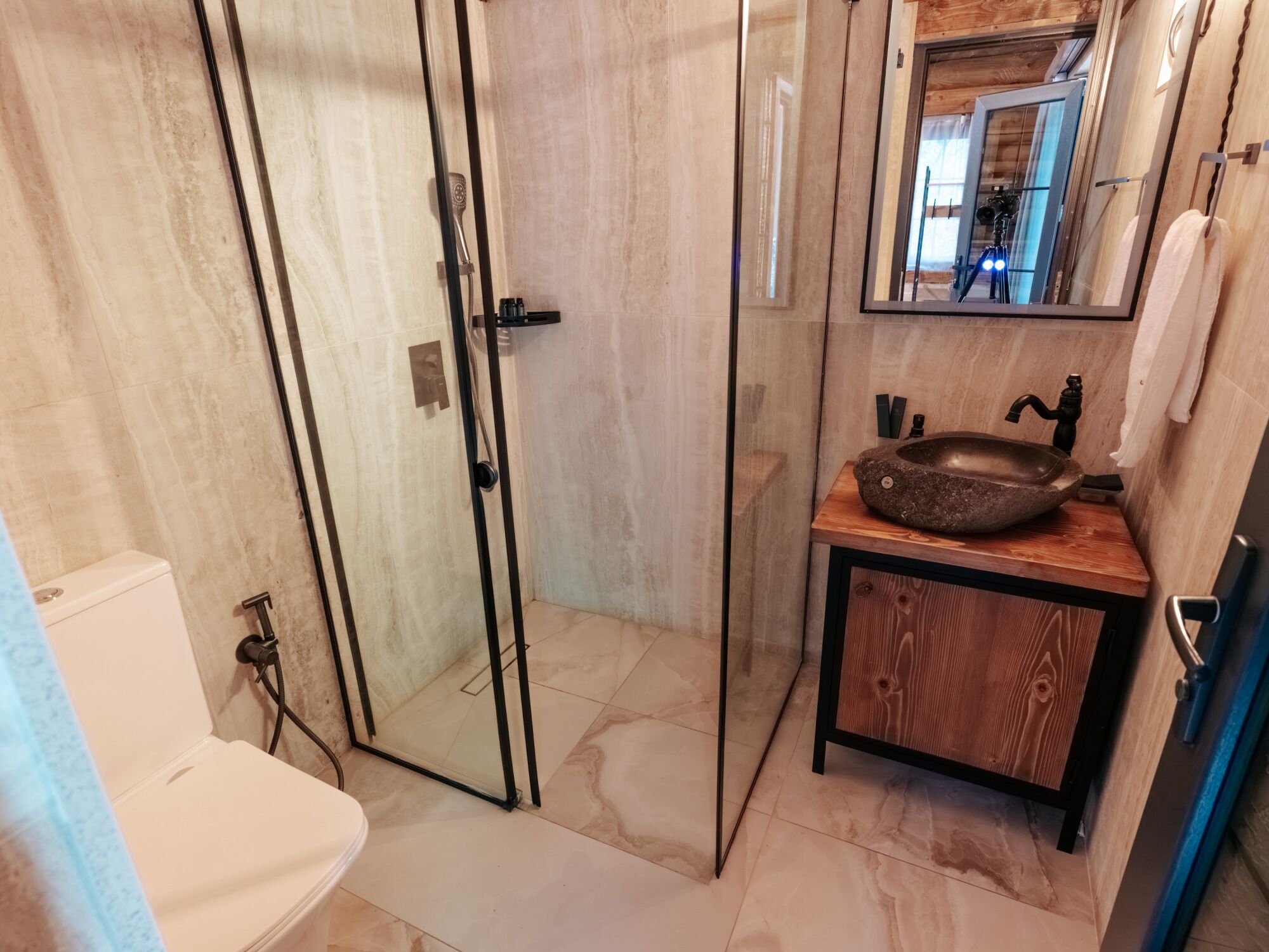 Et badeværelse med brusekabine i glas, et trækommode med en sten-vask og et hvidt toilet.