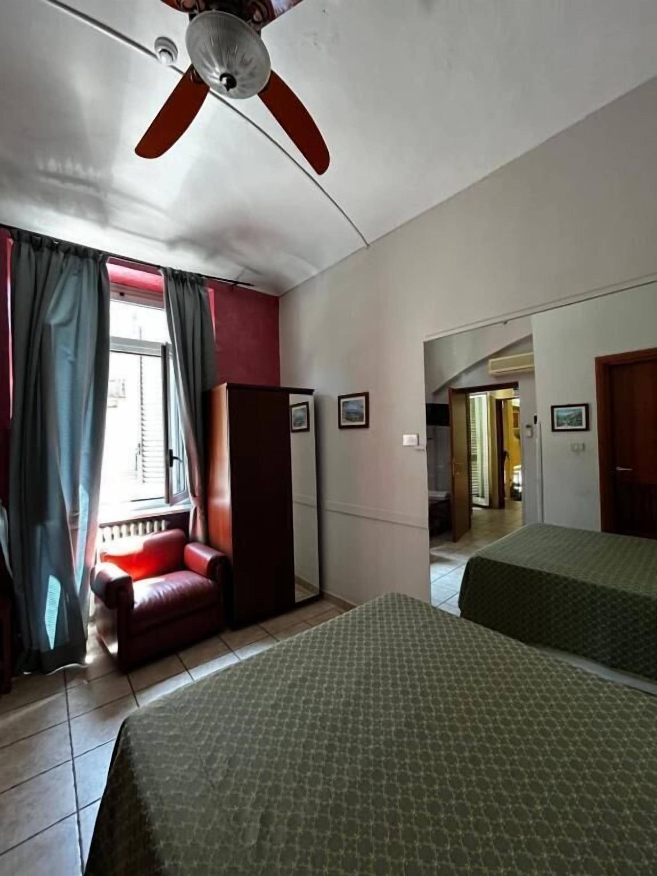 Une chambre d’hôtel avec un lit, une chaise, un ventilateur de plafond et une vue sur le couloir.