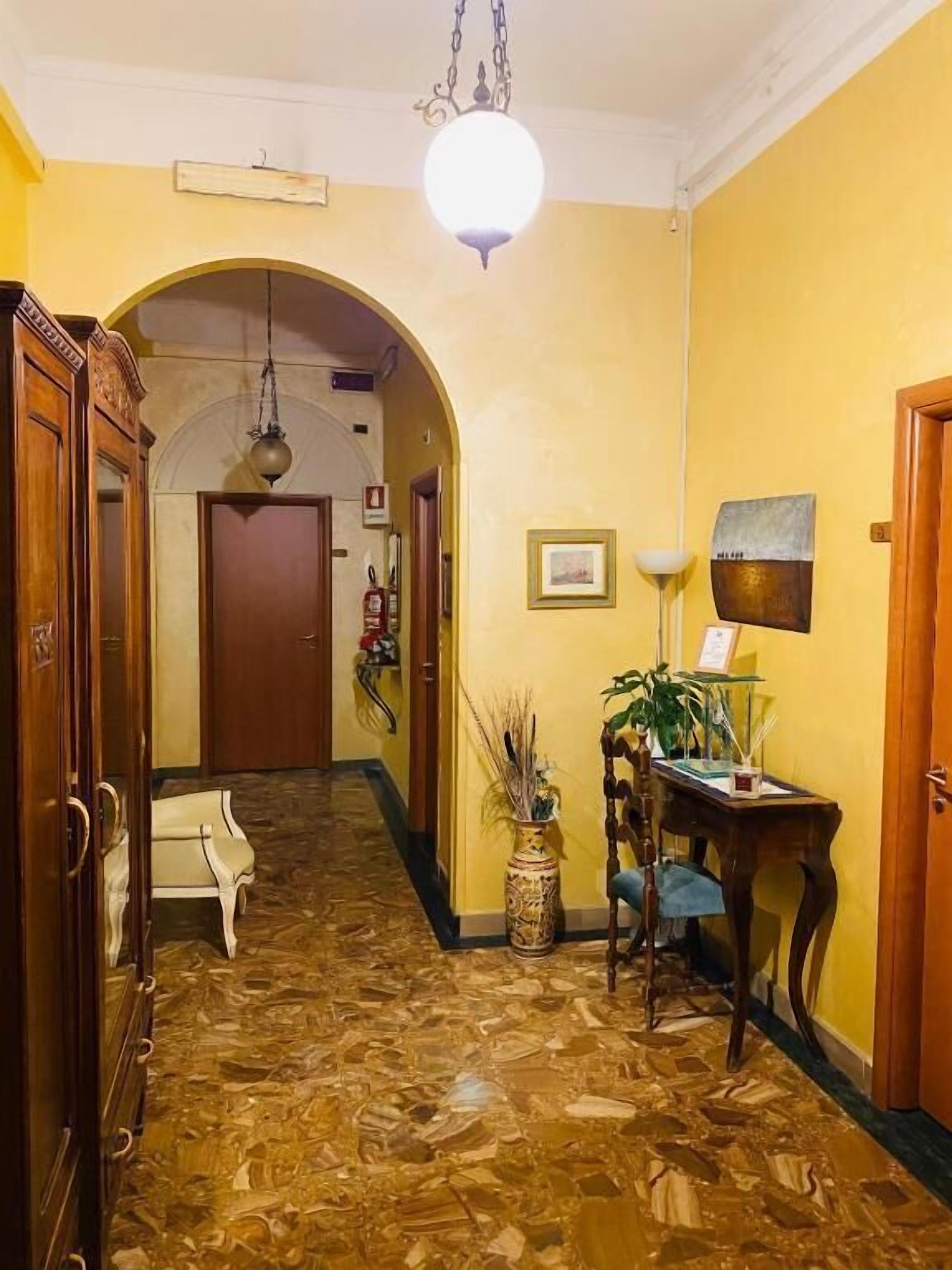 A hallway with a patterned floor, wooden furniture, a table with a lamp, and a door at the end.